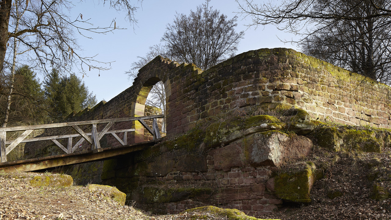 Mauer mit Durchgang und hölzernem Steg